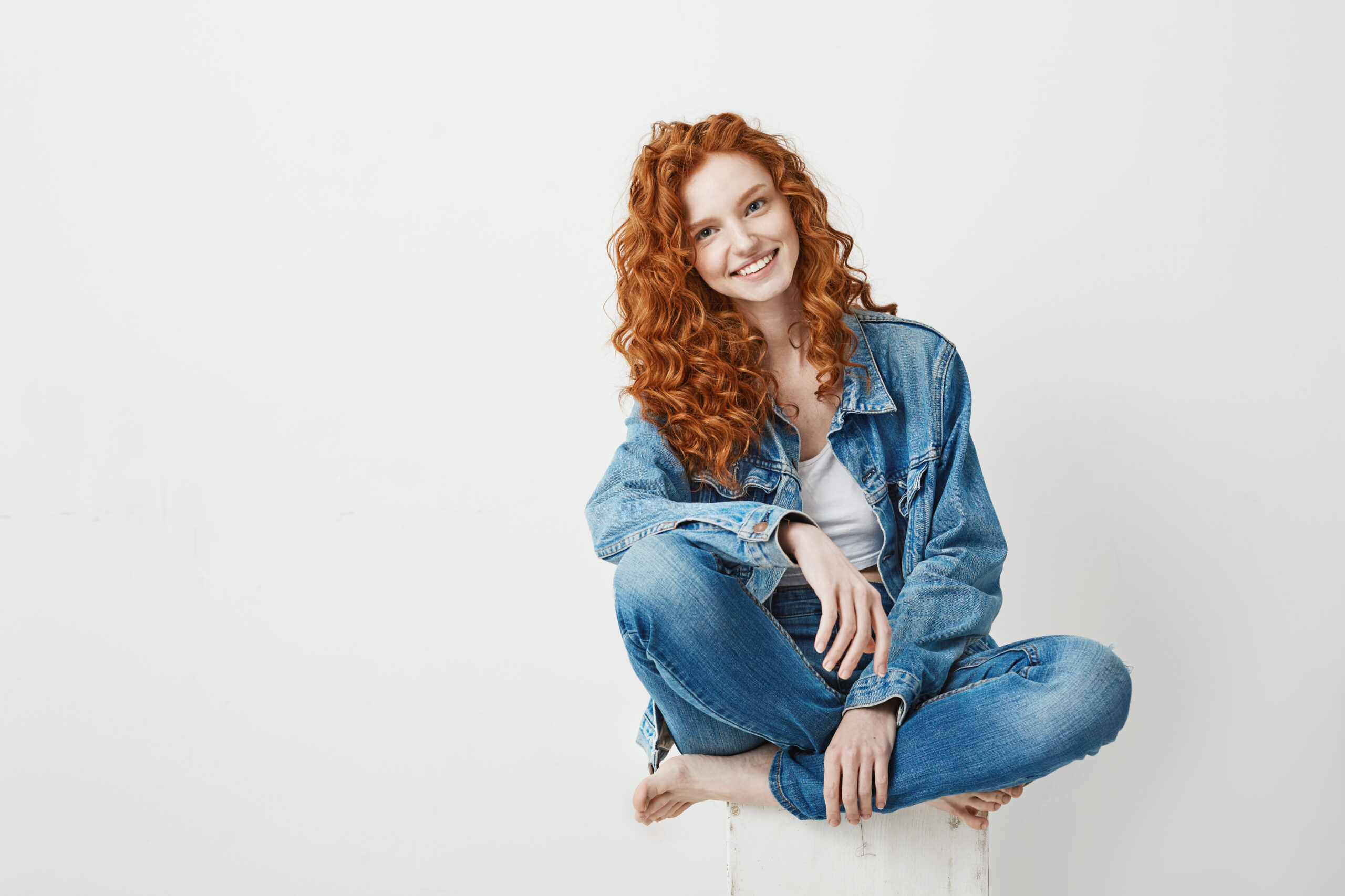 Young beautiful redhead girl smiling looking at camera sitting on box over white background. Copy space. с днем рождения олечка