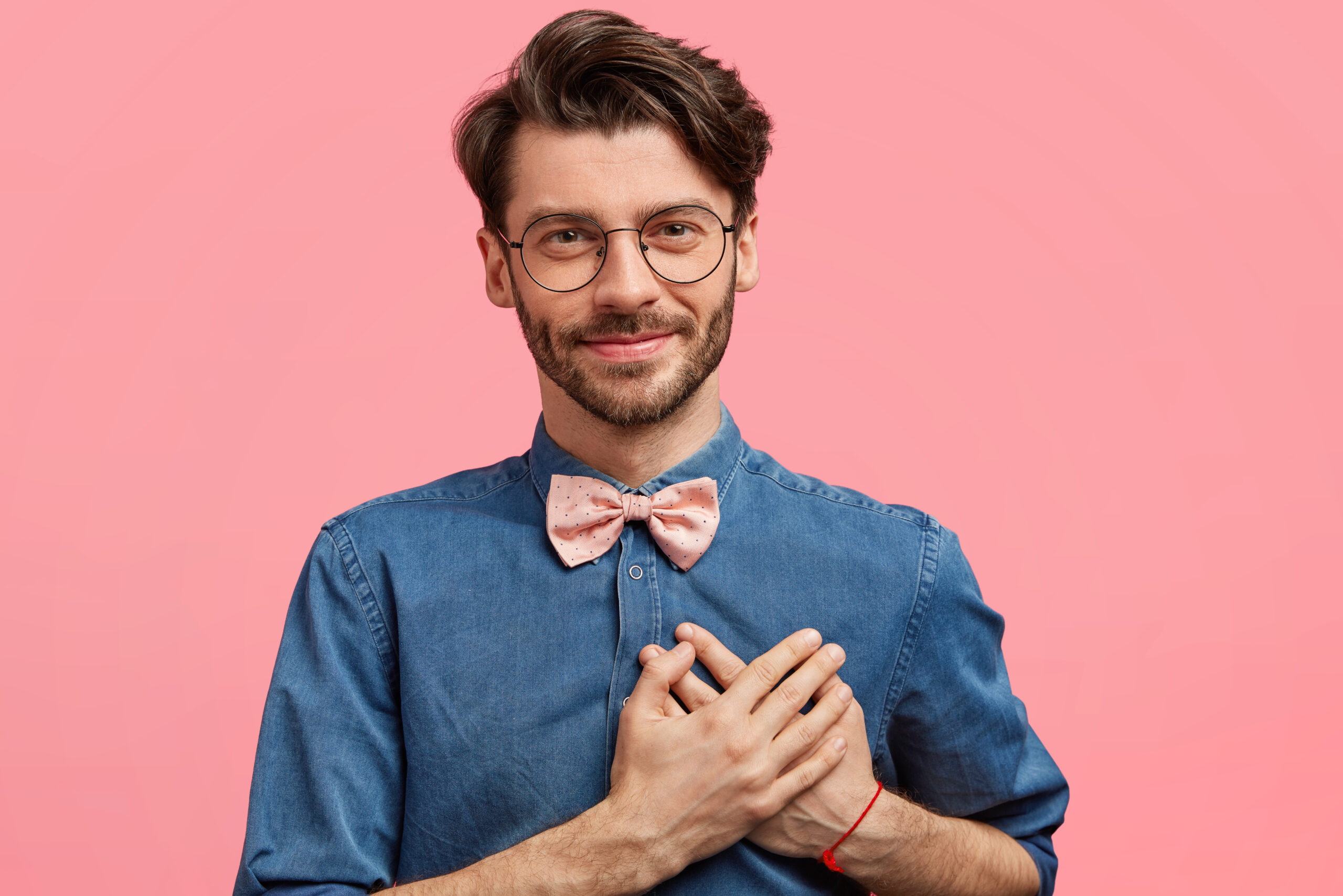 Photo of pleasant looking unshaven young male with pleased delighted look, keeps hands on heart, expresses love and devotion to girlfriend, isolated over pink background. People and emotions concept з днем народження сергій