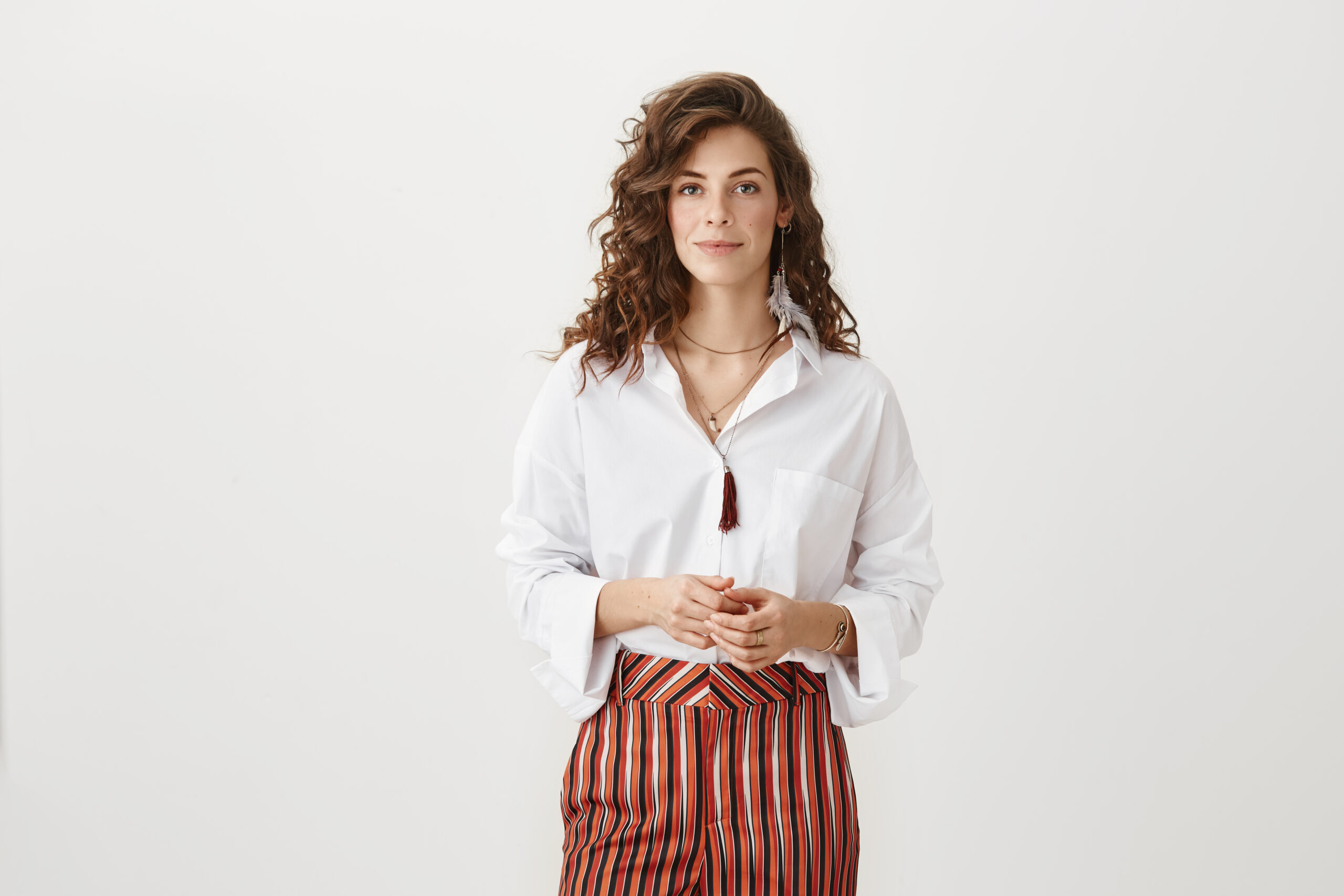How may I help you. Studio shot of fashionable adult female with stylish curly haircut, standing in fancy outfit over gray background, smiling while offering assistance to client з днем народження Надія
